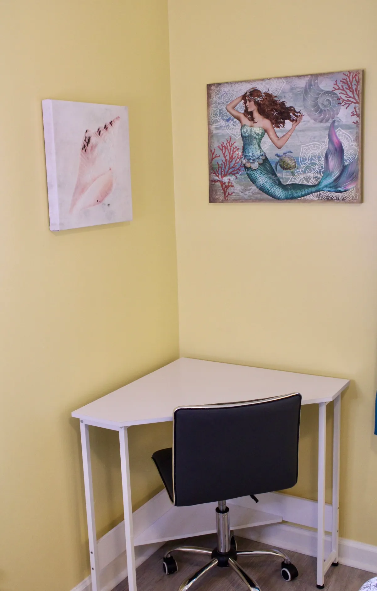 A corner workspace adorned with whimsical mermaid artwork and seashell painting, paired with a functional desk. The space is playful yet inspirational, offering a spot for creativity or planning local adventures.