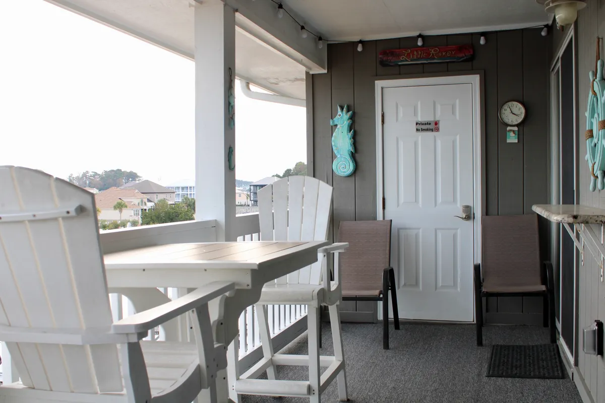 A cozy, inviting outdoor seating area with a white wooden table and two chairs, accented by playful seahorse decorations. The area feels intimate and perfect for enjoying morning coffee or evening drinks while overlooking the water.