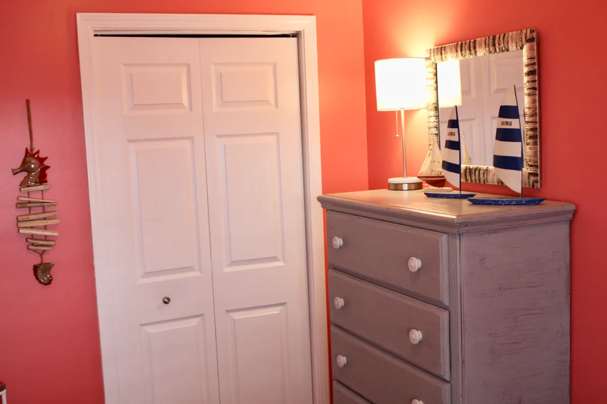 A charming, light-filled corner with a gray dresser, decorative mirror, and sailboat-inspired decor. The setting is playful and inviting, evoking the nearby waterfront and the peacefulness of coastal living.