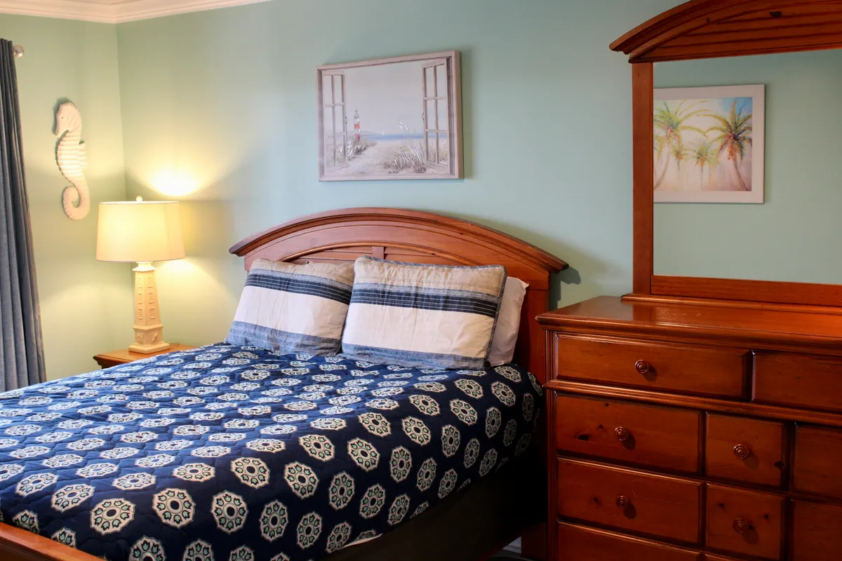 A serene bedroom with a comfortable bed, soft lighting from a bedside lamp, tasteful wall art, and a dresser. The ambiance is soothing and uncluttered, inviting restful sleep and moments of relaxation.