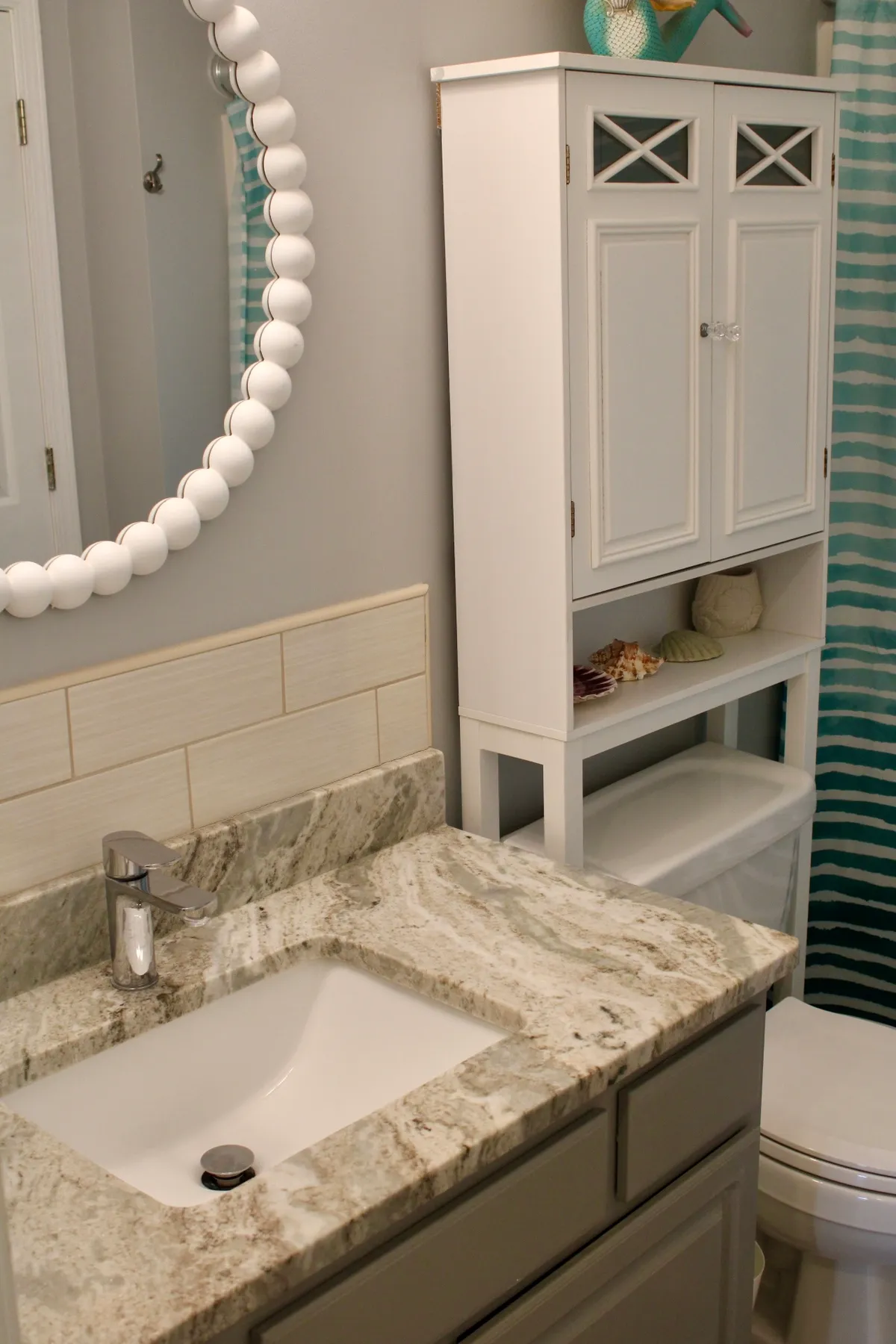 A sparkling bathroom with a granite countertop, white cabinetry, a decorative mirror, and a shower curtain. The room feels fresh and inviting, ideal for morning routines or unwinding after a day at the beach.